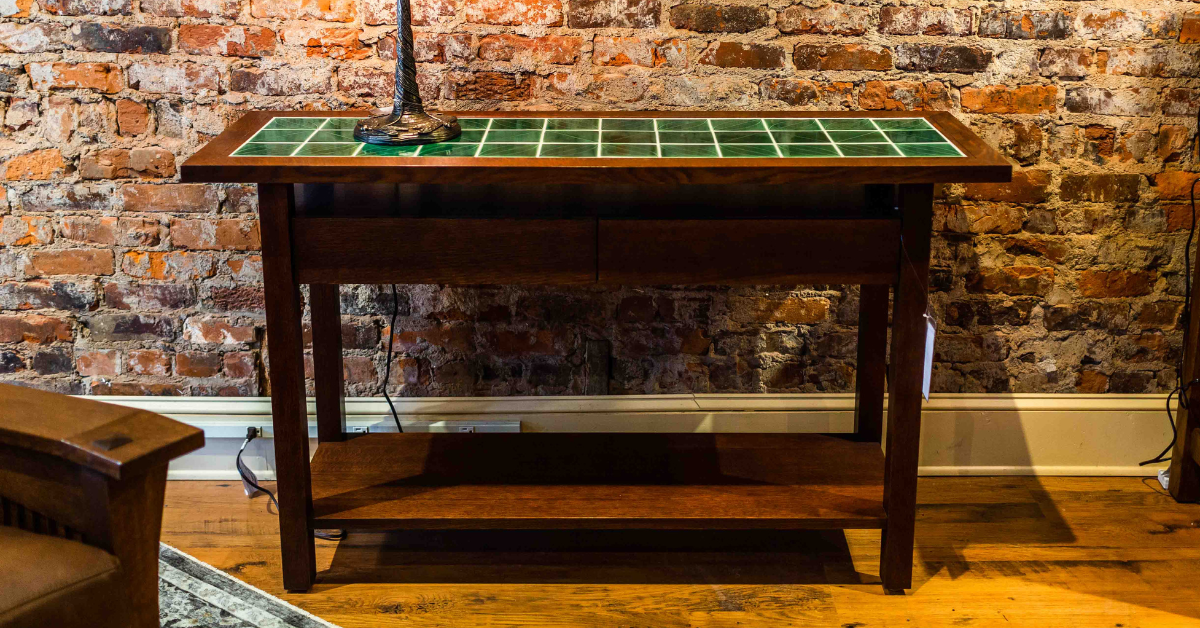 A green top console table with a wooden base in front of a brick wall