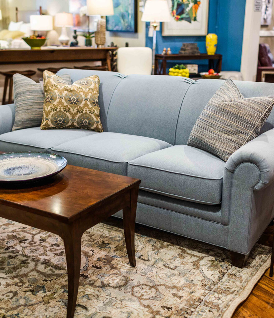 A blue couch with 3 pillows on top and a brown coffee table with a plate on top of it
