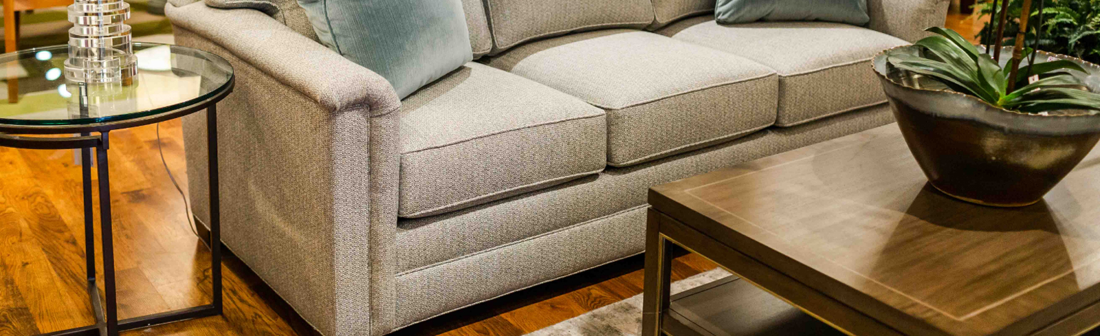 A beige colored couch with two pillows on it, an coffee table in front, and an end table to the right of it.