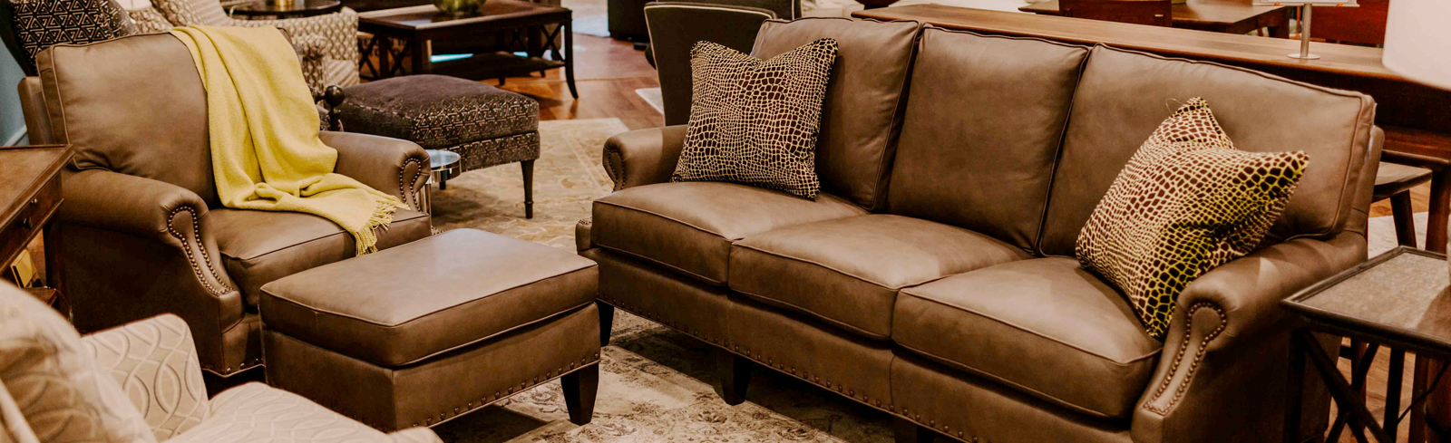 A brown couch with two pillows and a brown chair with a yellow blanket on it